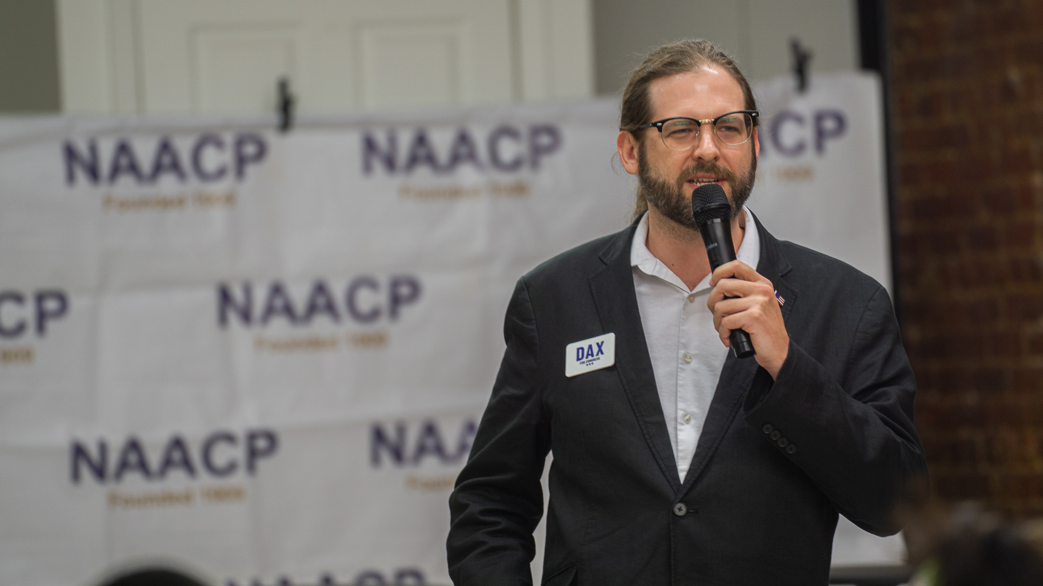 Candidate addressing the room with microphone at NAACP backdrop