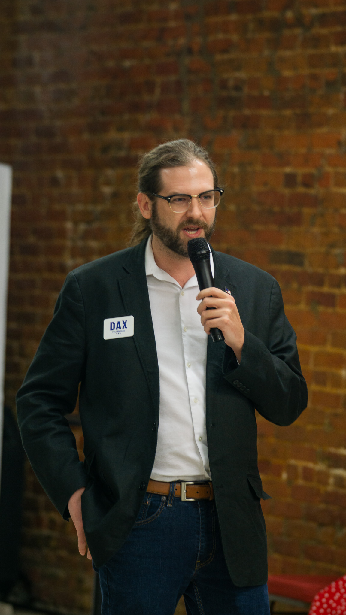 Candidate speaking with microphone against a brick wall backdrop