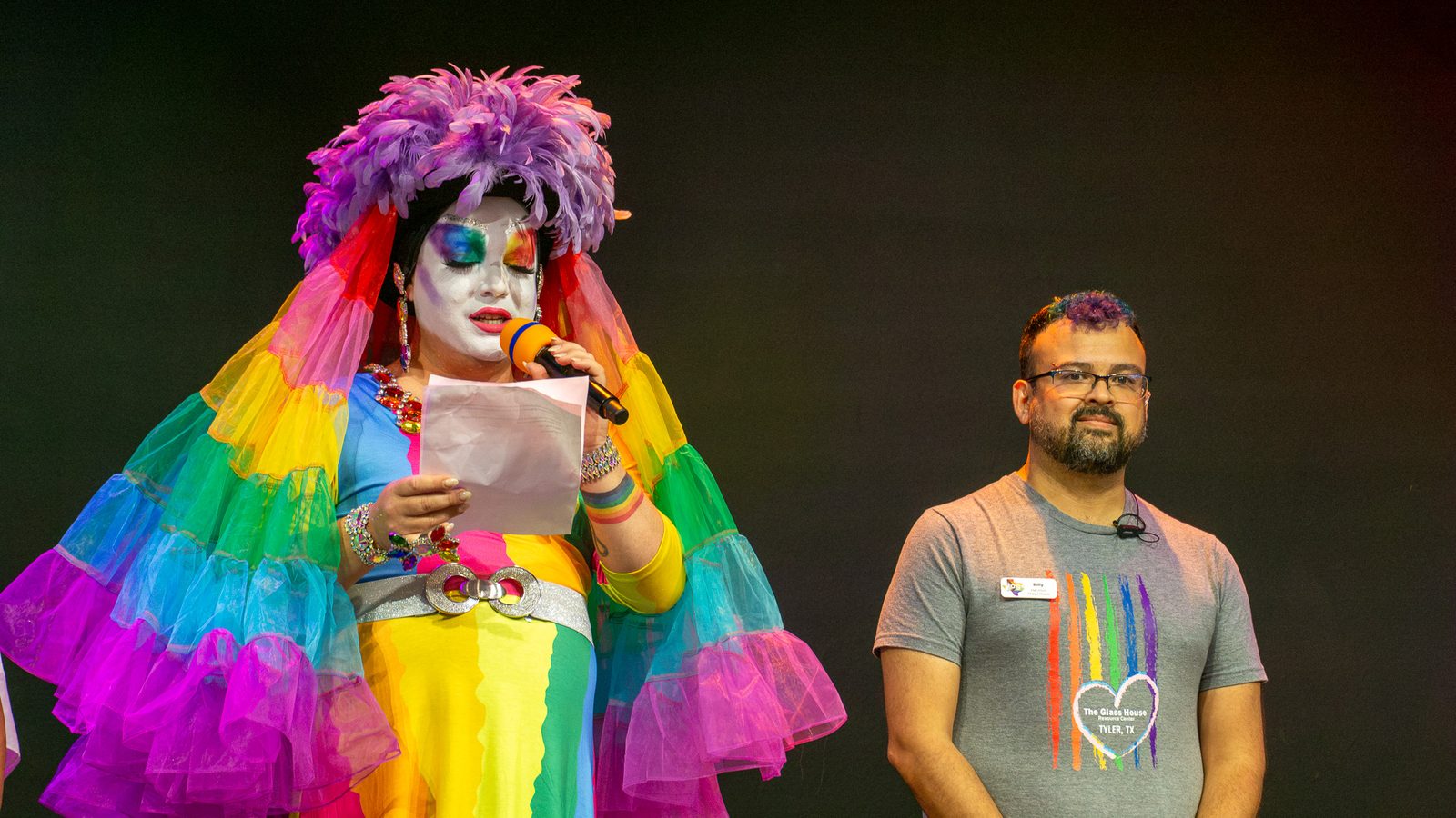 Performer in a rainbow fringe outfit and wig greeting the crowd