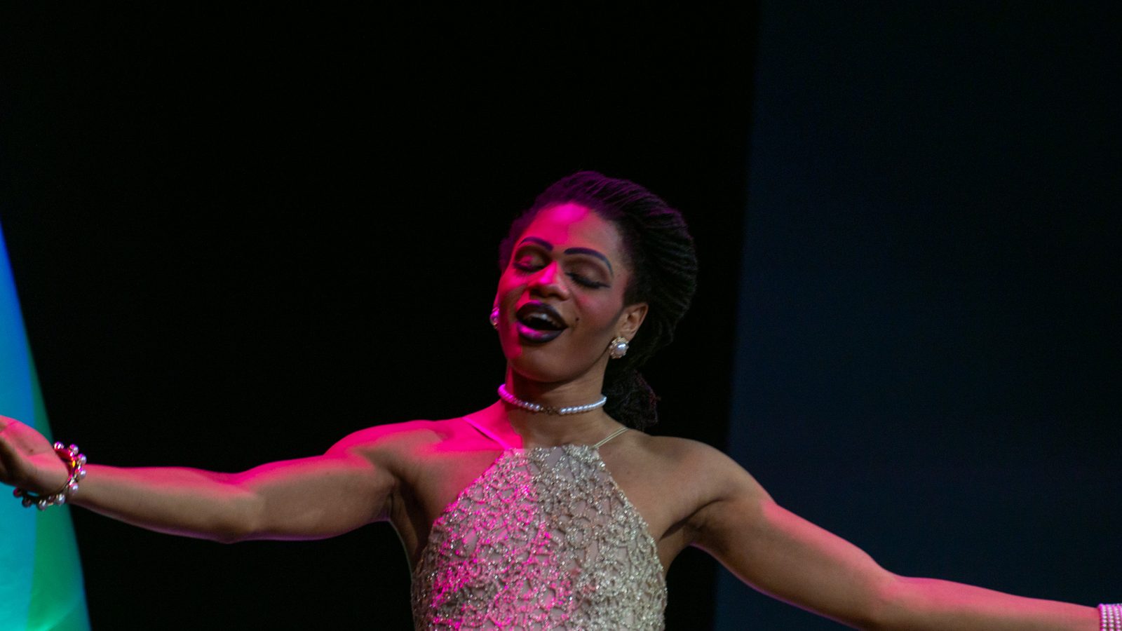 Drag performer in an elegant pale gown on a spotlit stage