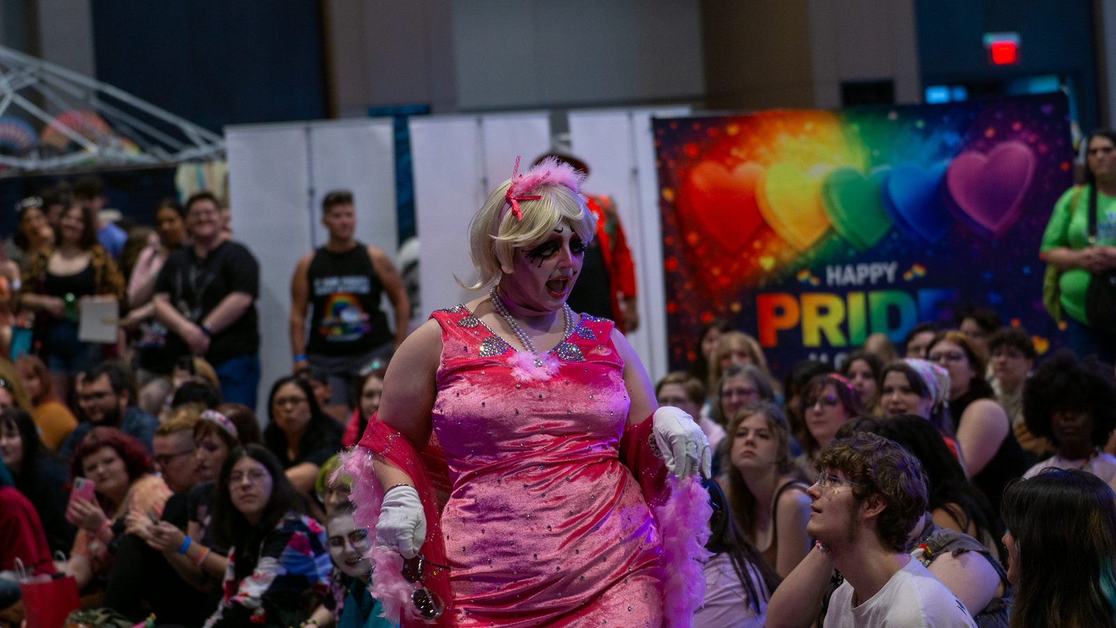 Drag performer in a pink gown working the crowd in front of a Happy Pride banner