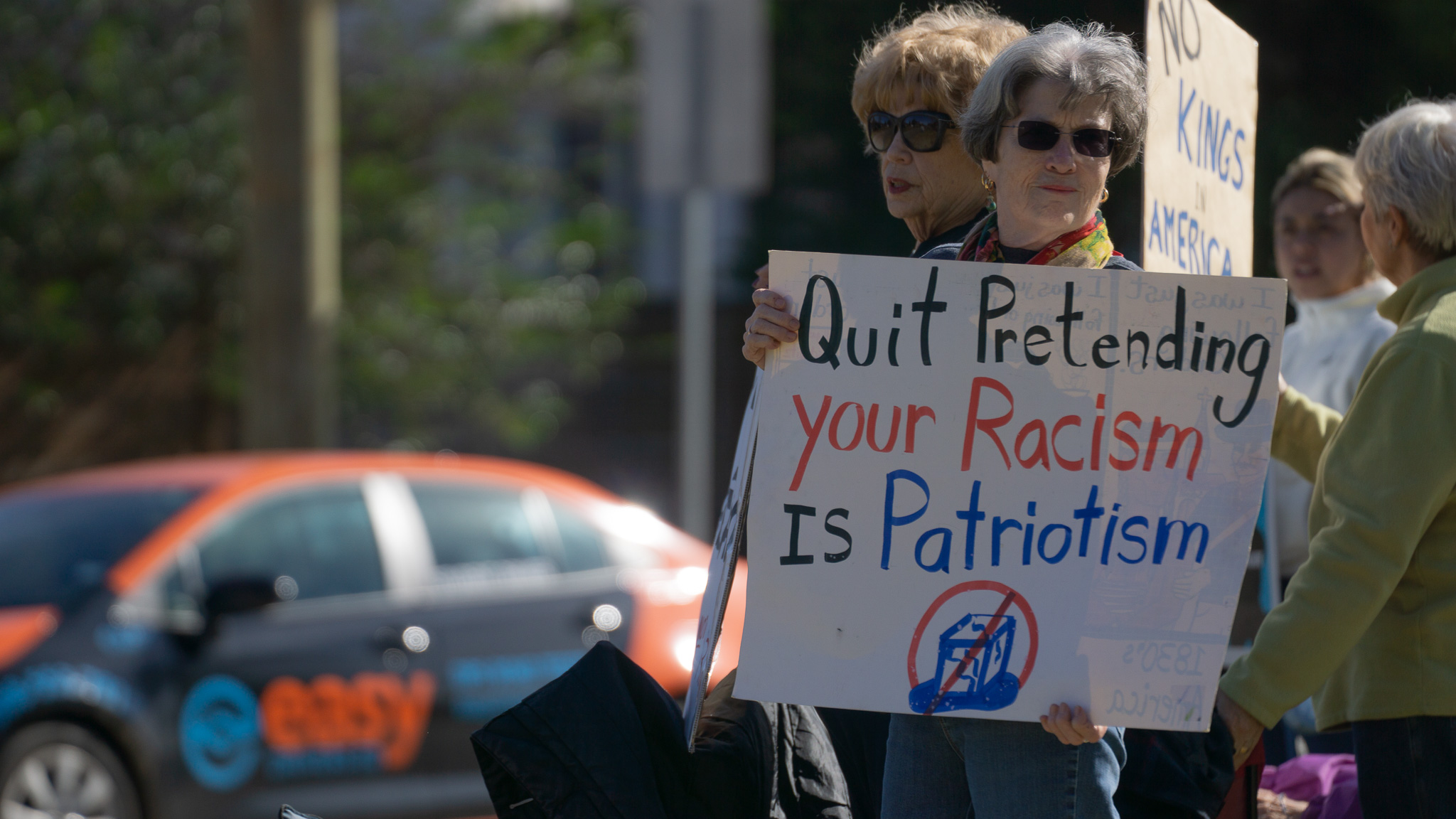 Two women holding Quit Pretending Your Racism Is Patriotism sign
