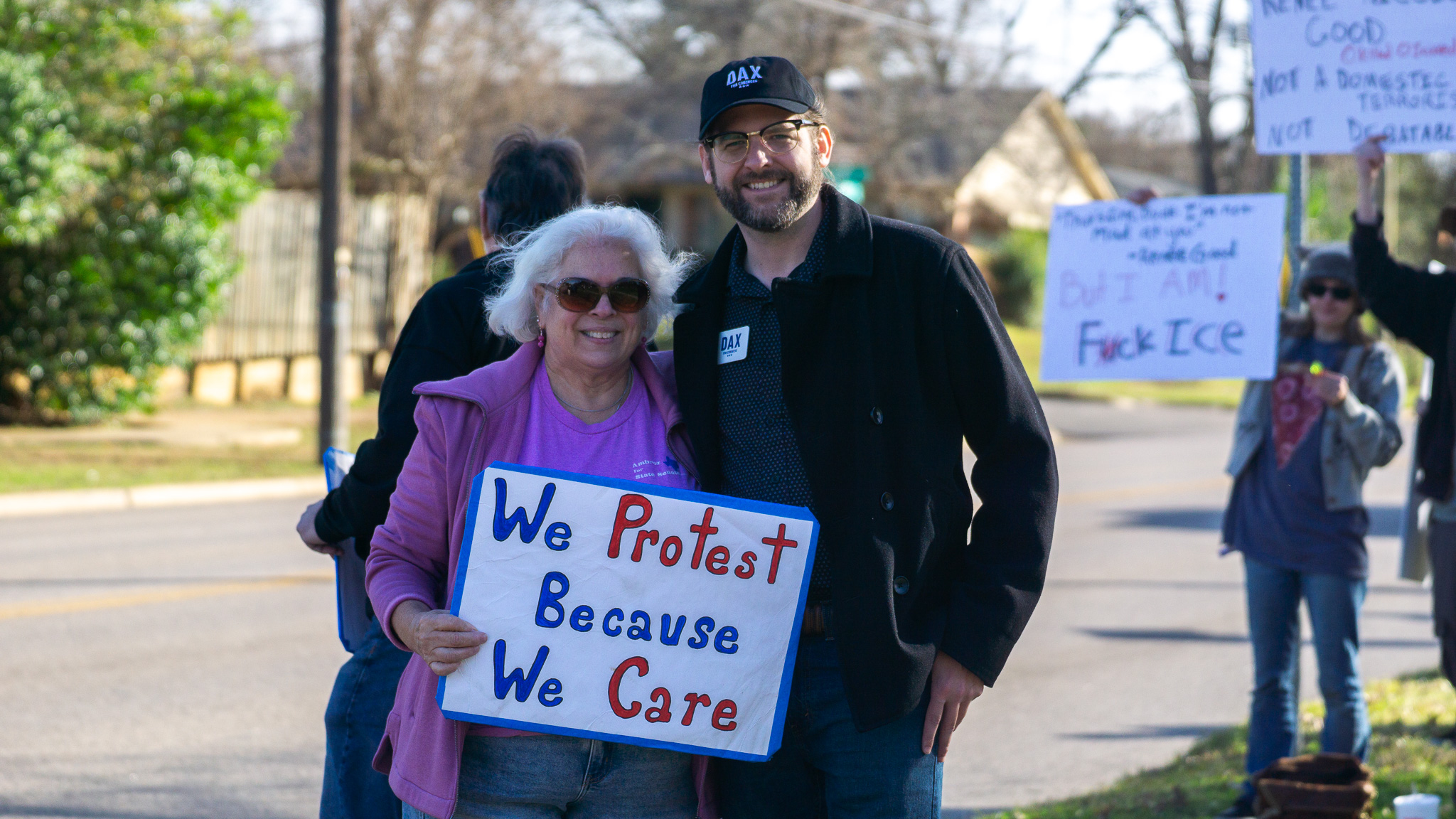 Local candidate with supporter holding We Protest Because We Care sign
