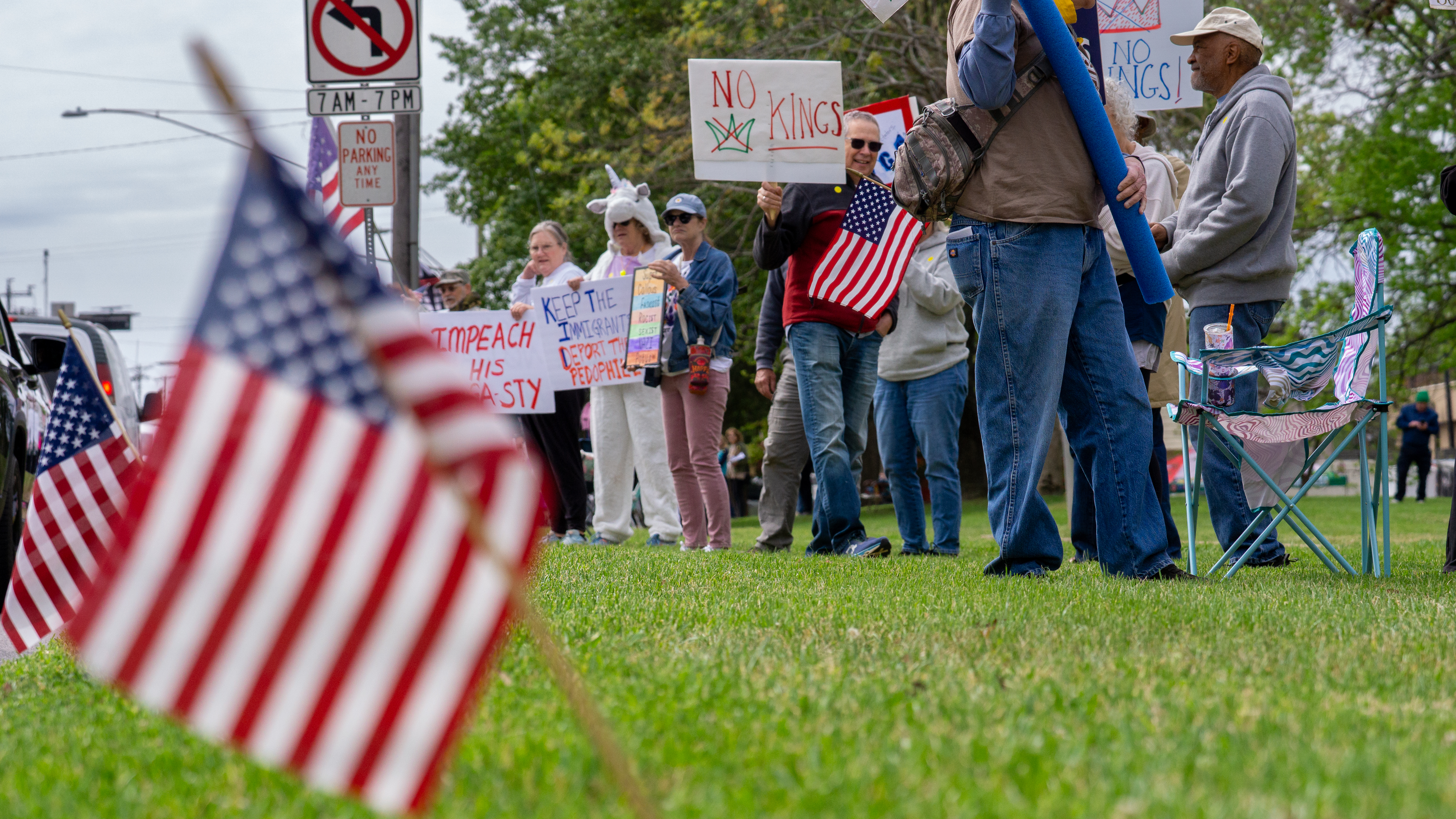 Wide crowd of protesters lining a street with American flags in the foreground