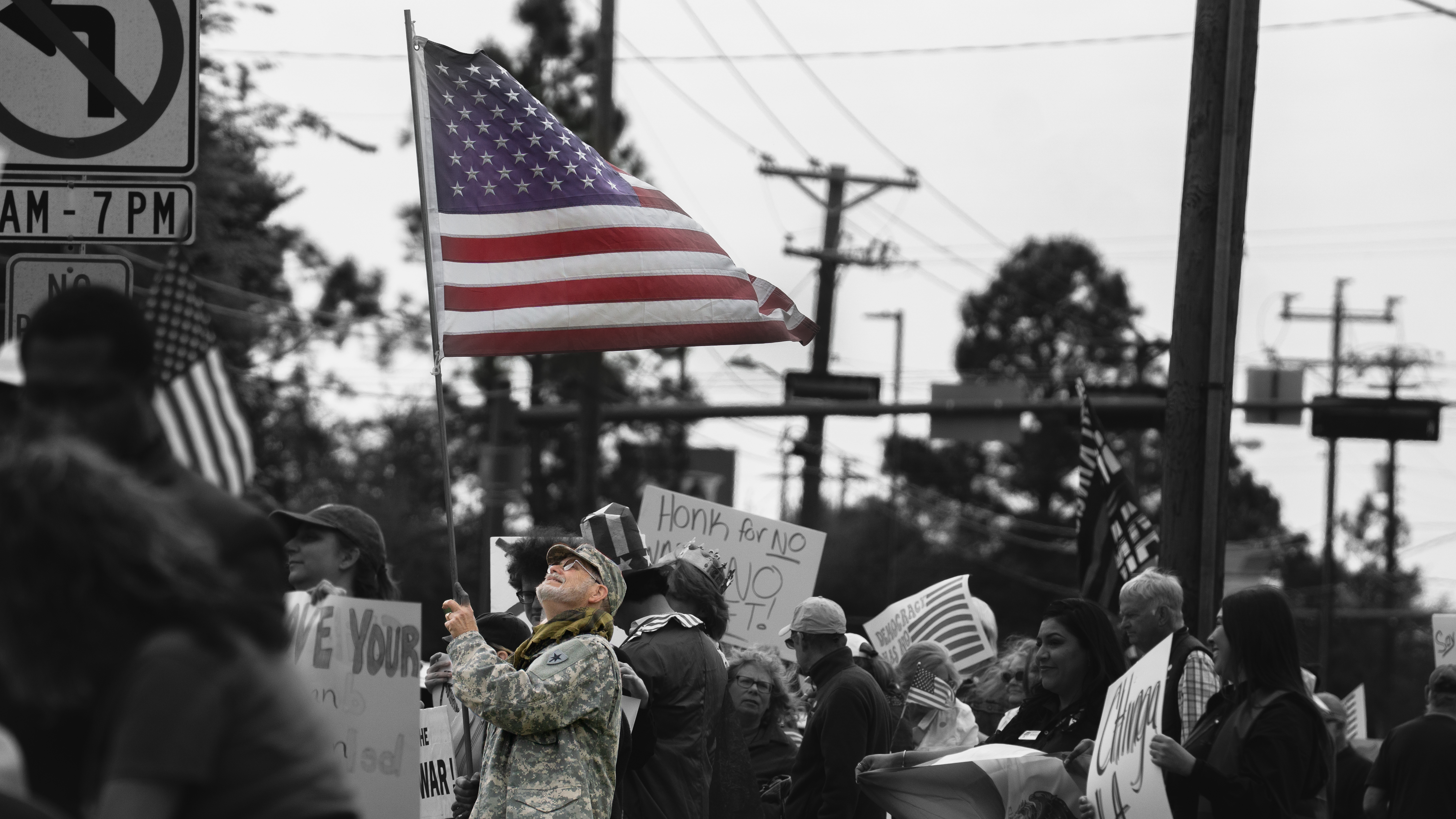 Veteran waving American flag above a sea of protesters in black and white