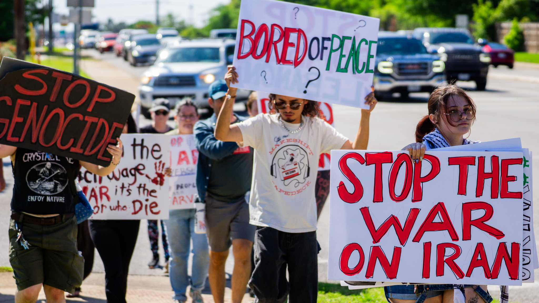Marchers in motion down the street carrying Stop Genocide and Stop the War on Iran signs
